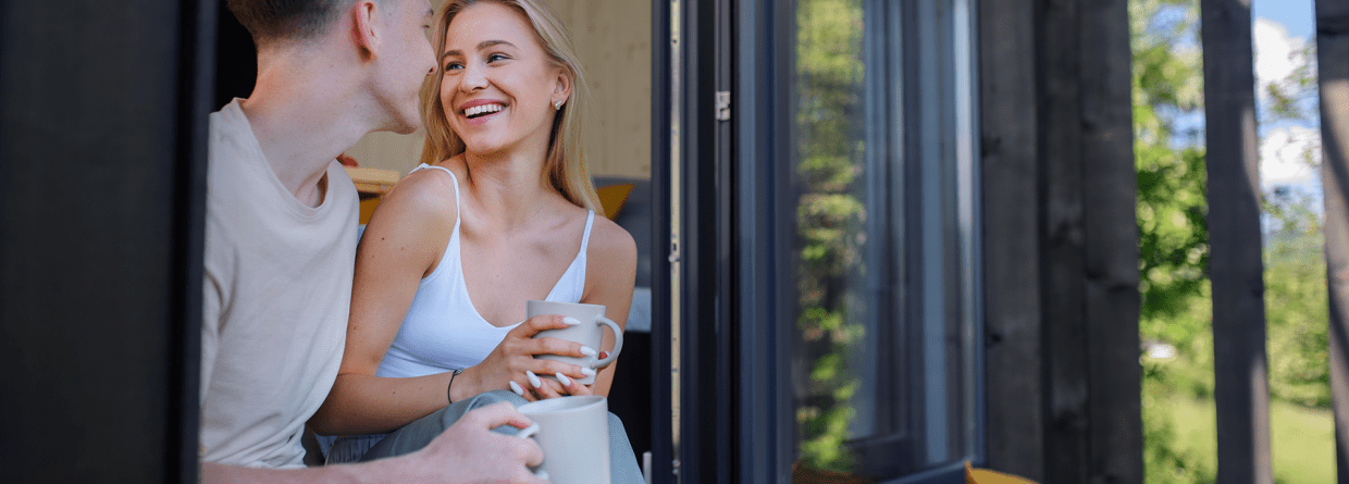 Jong stel drinkt in de deuropening van hun nieuwe huis koffie en knuffelenuffel