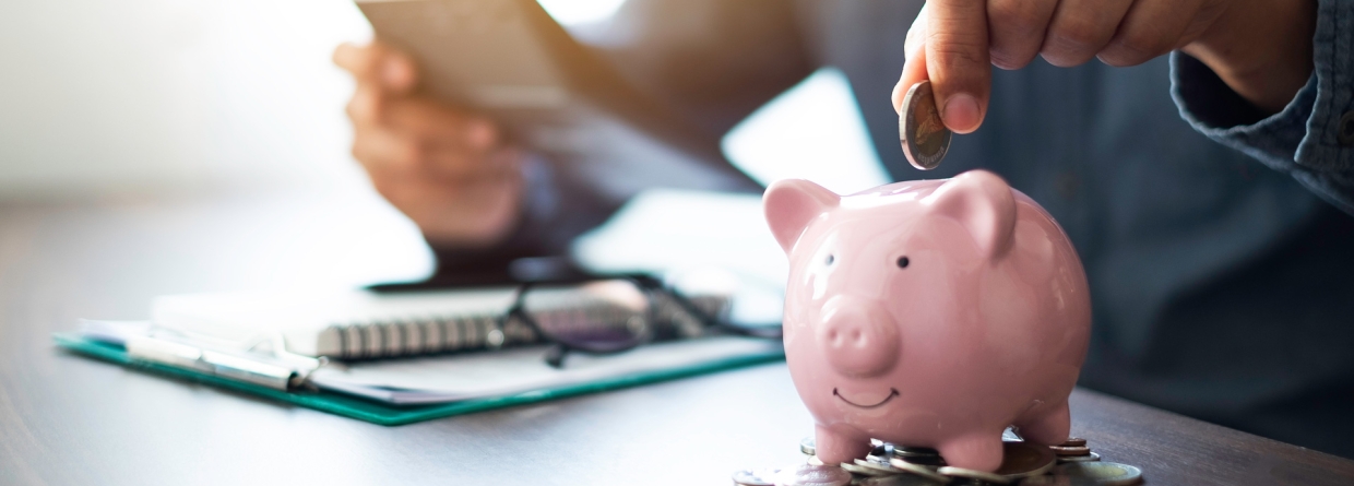 Een mannenhand die munten in een roze spaarpot stopt om geld te sparen